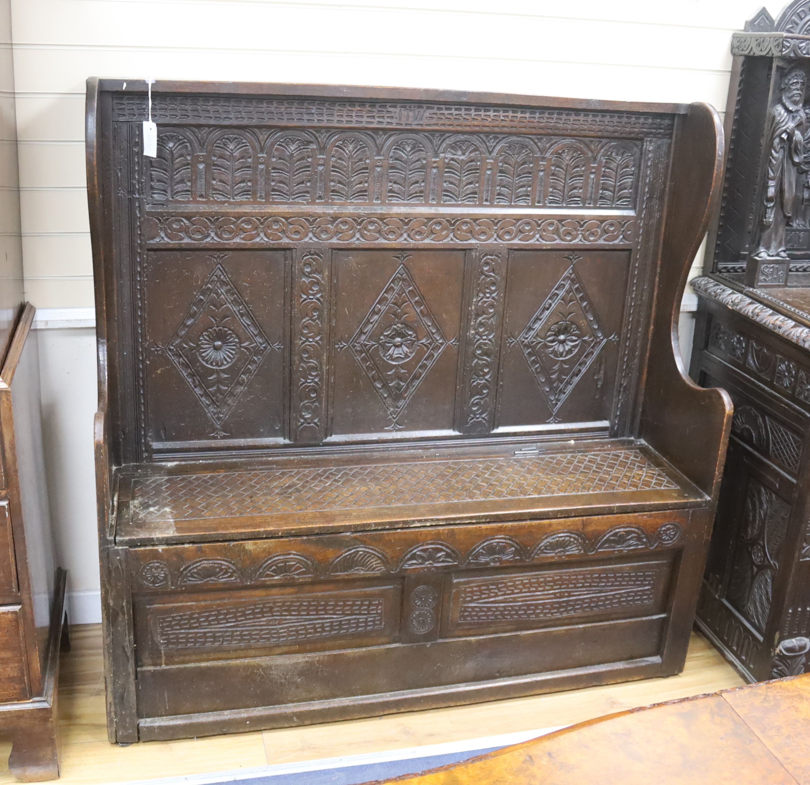 An 18th century and later carved oak settle with hinged box seat, width 137, depth 42, height 137 cms.